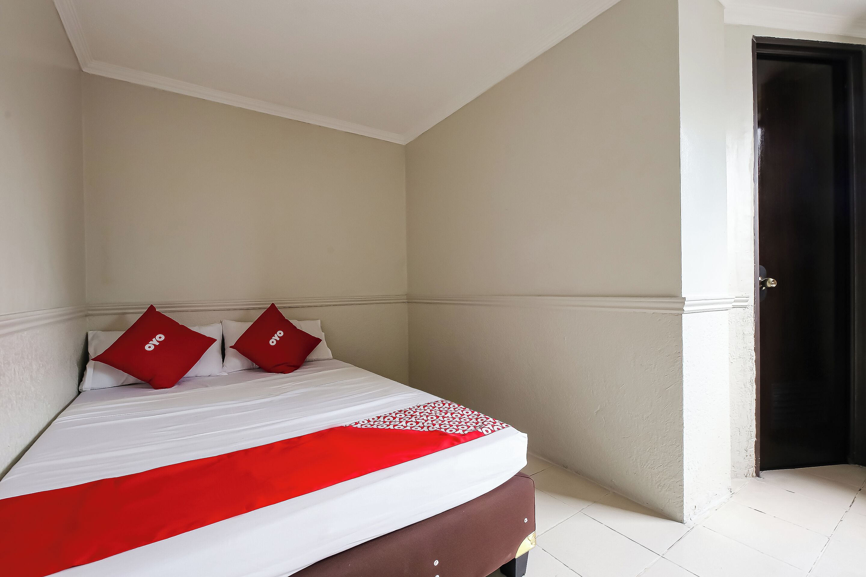 Un lit bien fait, recouvert d’une couvre-lit blanche et rouge, avec deux oreillers rouges et une tête de lit marron.