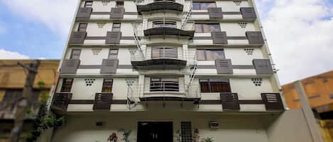 A multi-story building with a central entrance, balconies, and potted plants.