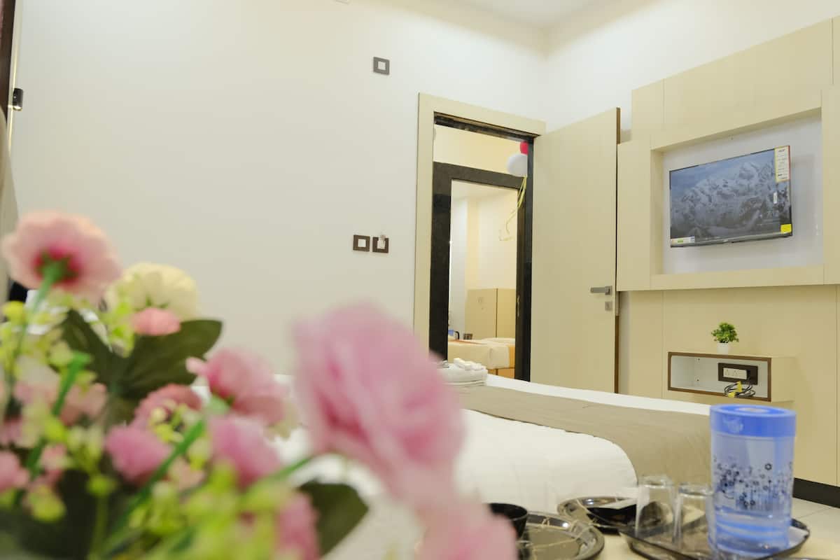 A hotel room with a bed, a TV mounted on the wall, a small table with a water bottle, and a mirror reflecting the room.