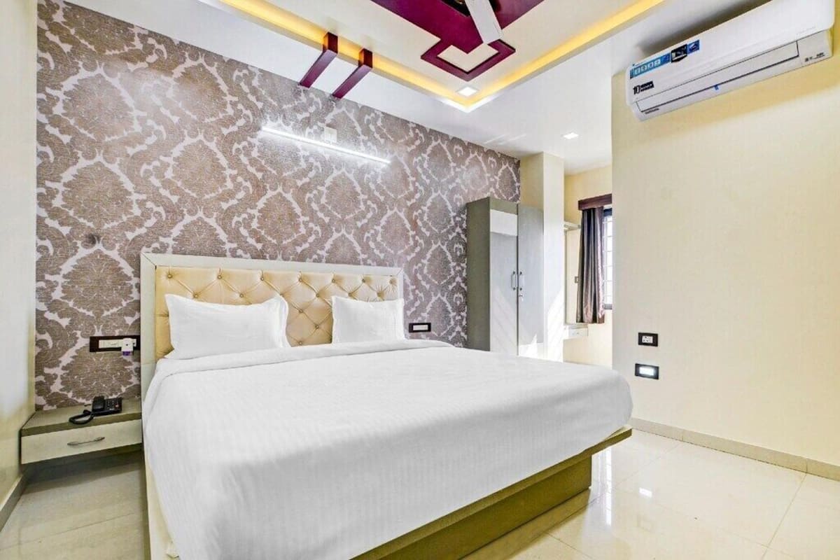 A modern hotel room with a large bed, patterned wallpaper, and an air conditioning unit.