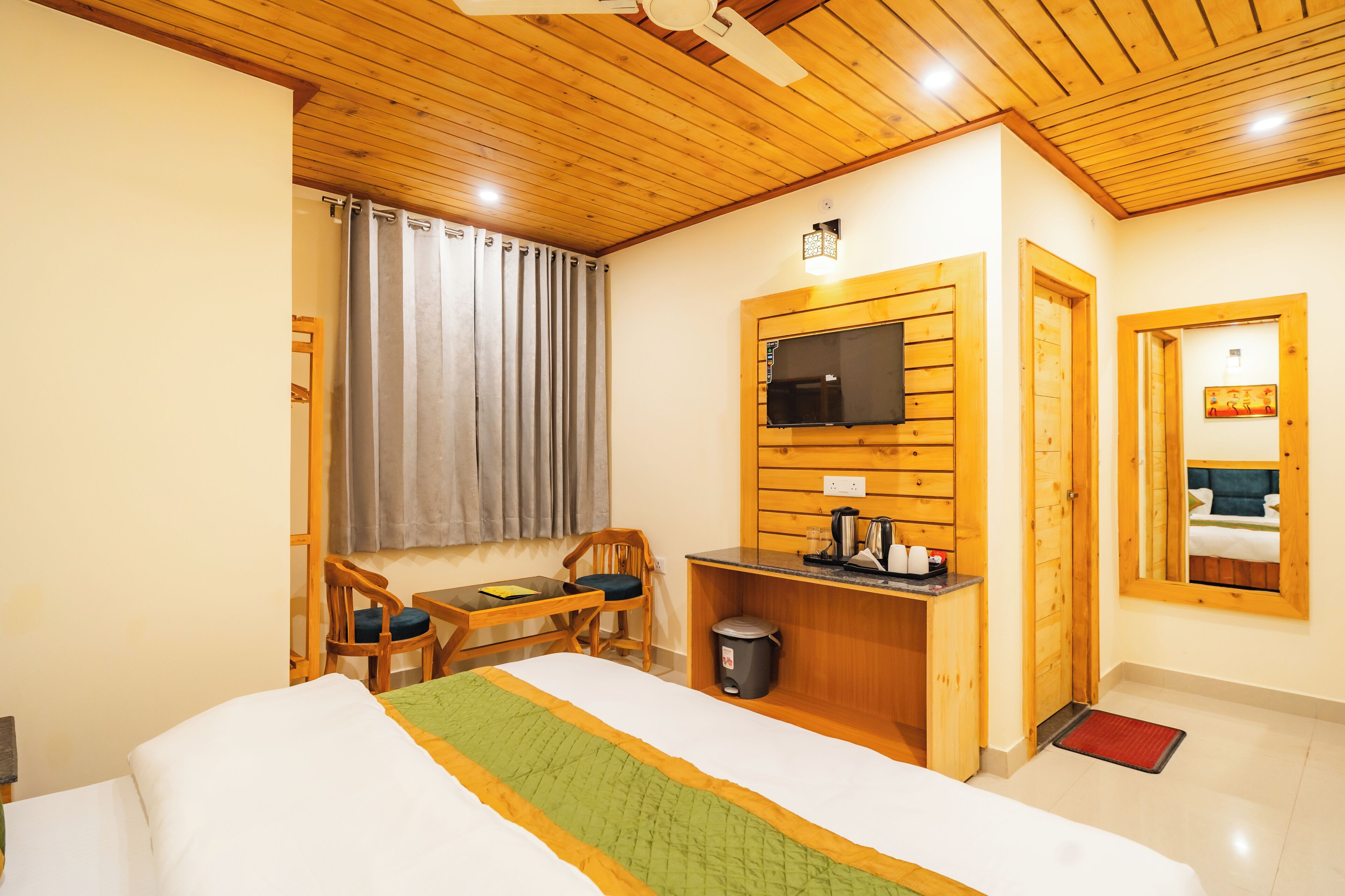 Une chambre d’hôtel comprenant un lit, un bureau avec une chaise, un téléviseur fixé au mur et une fenêtre avec des rideaux.