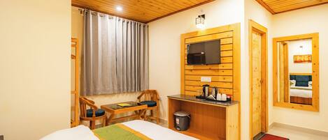 A hotel room with a bed, a desk with a chair, a TV mounted on the wall, and a window with curtains.