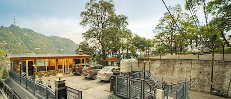 A hotel with a rooftop terrace, a parking area, and a view of a hilly landscape.