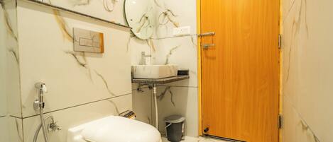 A bathroom with a toilet, sink, shower, and a wooden door.