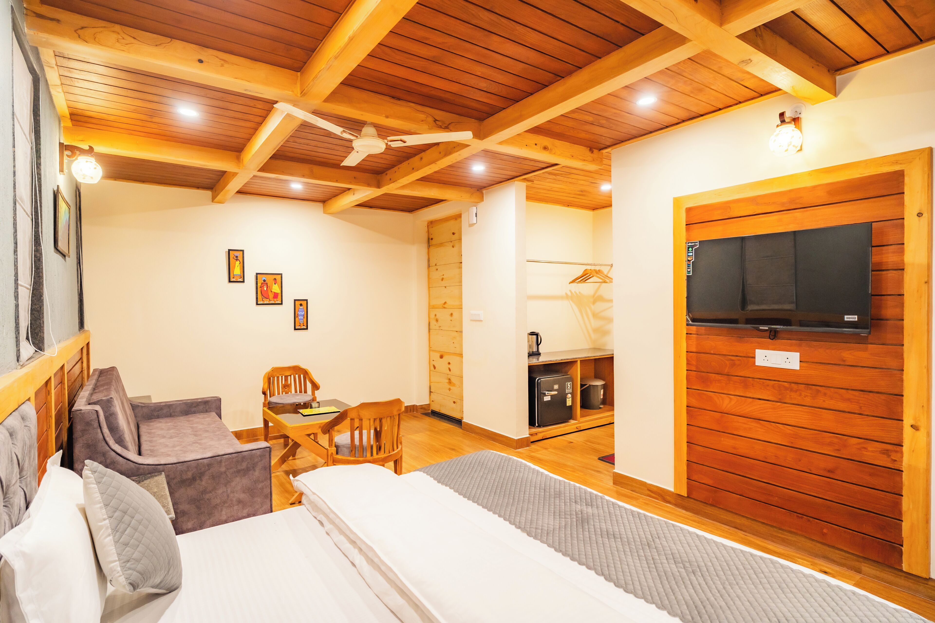 Ein gemütliches Zimmer mit einem Bett, einer Couch, einem Holztisch und einem an der Wand befestigten Fernseher.
