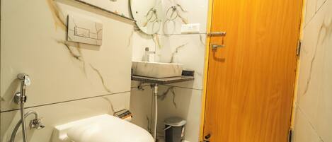 Un baño con inodoro, lavamanos, espejo, ducha y puerta de madera.