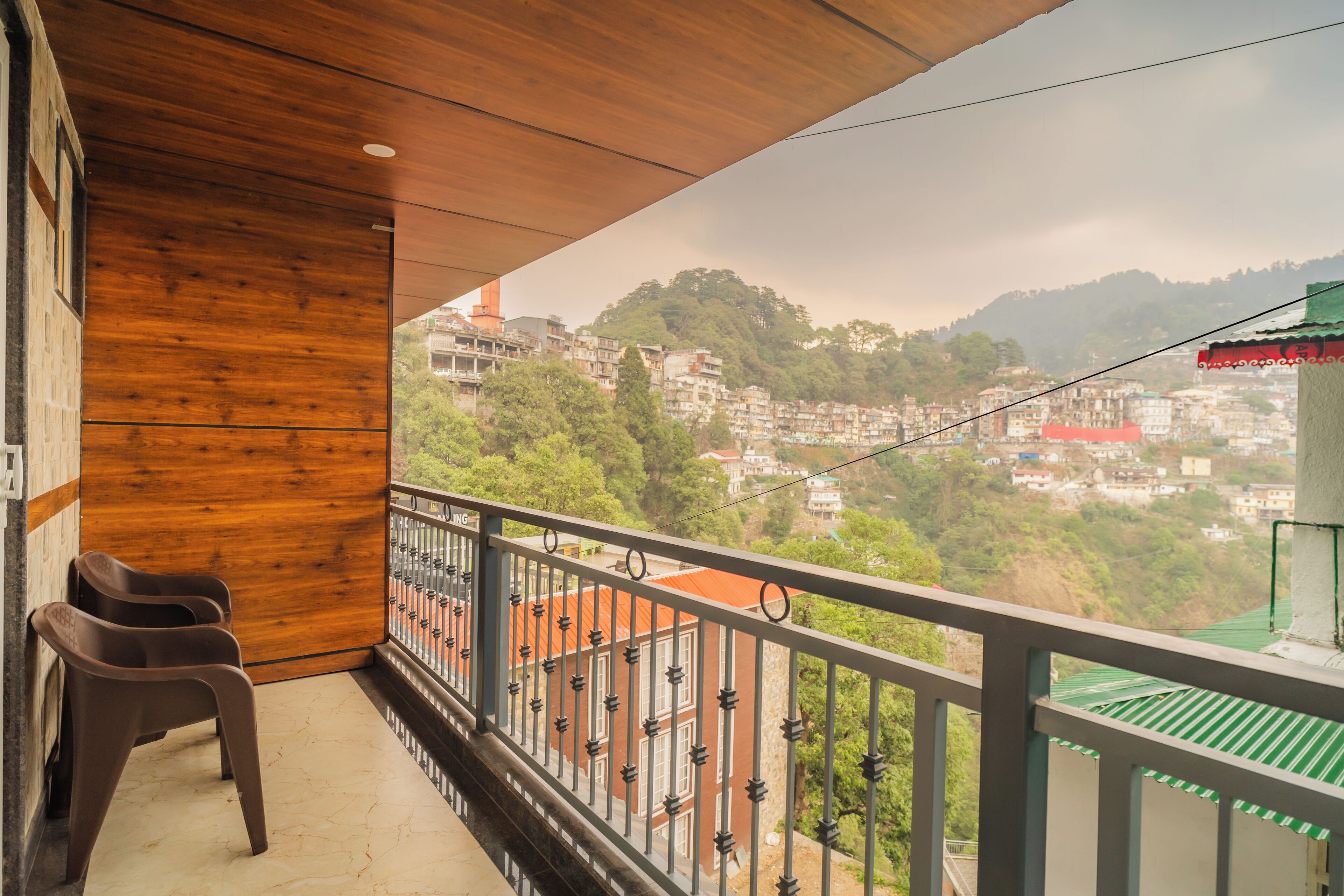 A balcony with a view of a hillside town, wooden walls, and a metal railing.