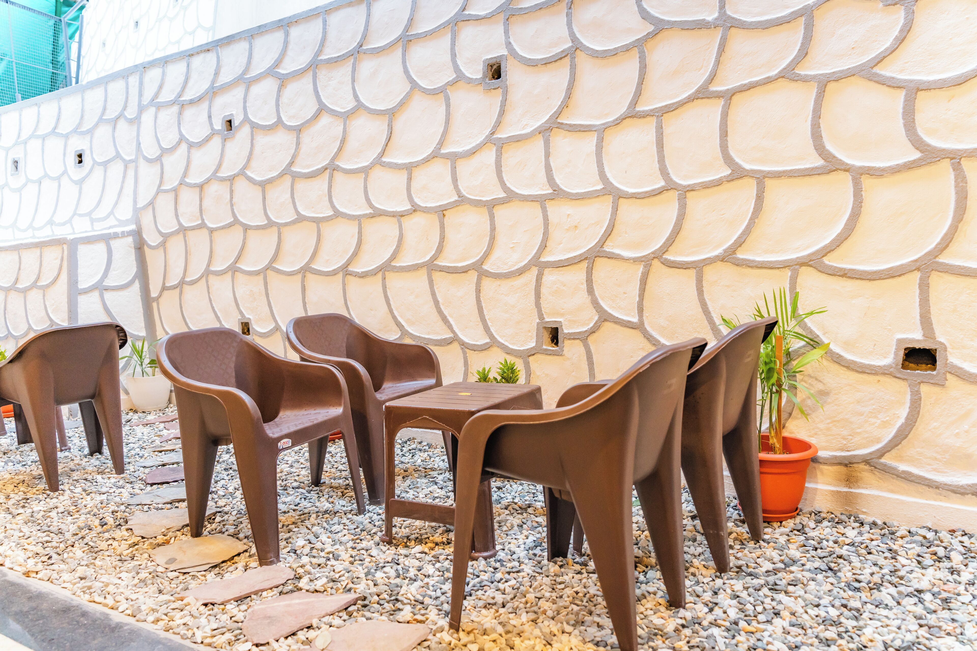 Una zona de estar con sillas y mesas de plástico, una pared decorativa con motivo de escamas de pez y plantas en macetas.