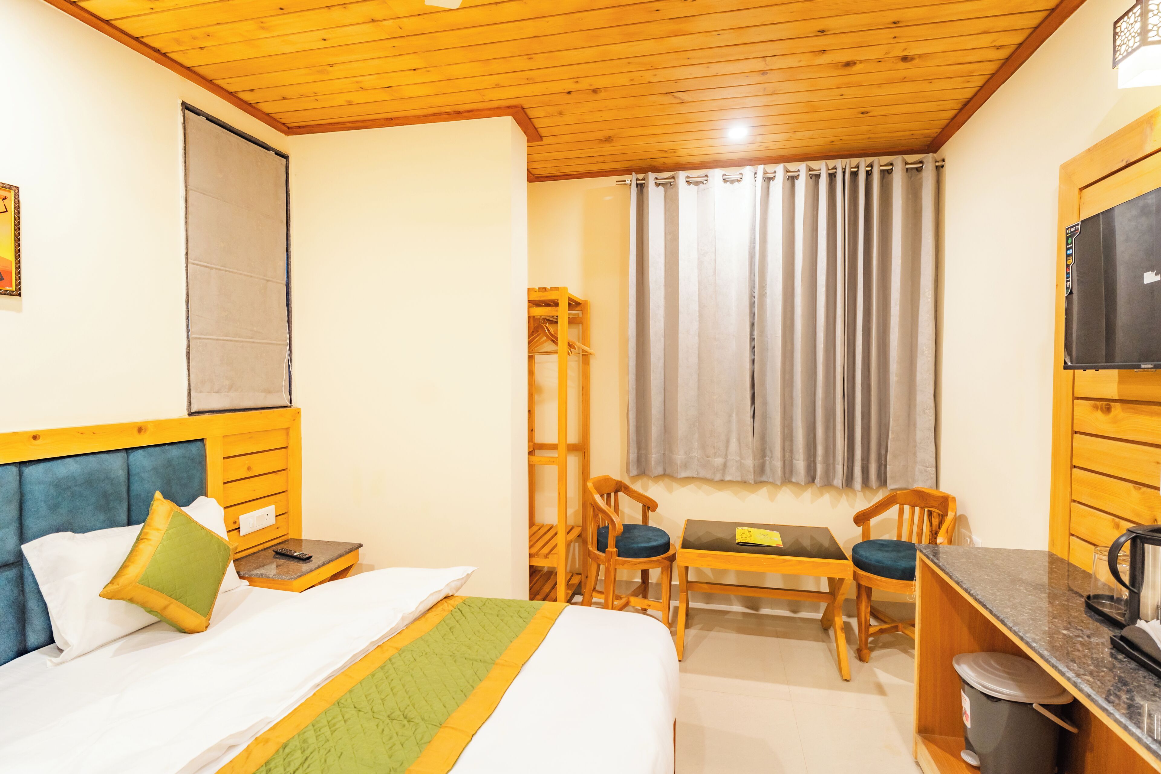 A hotel room with a bed, a desk, a chair, a TV, and a window with curtains.