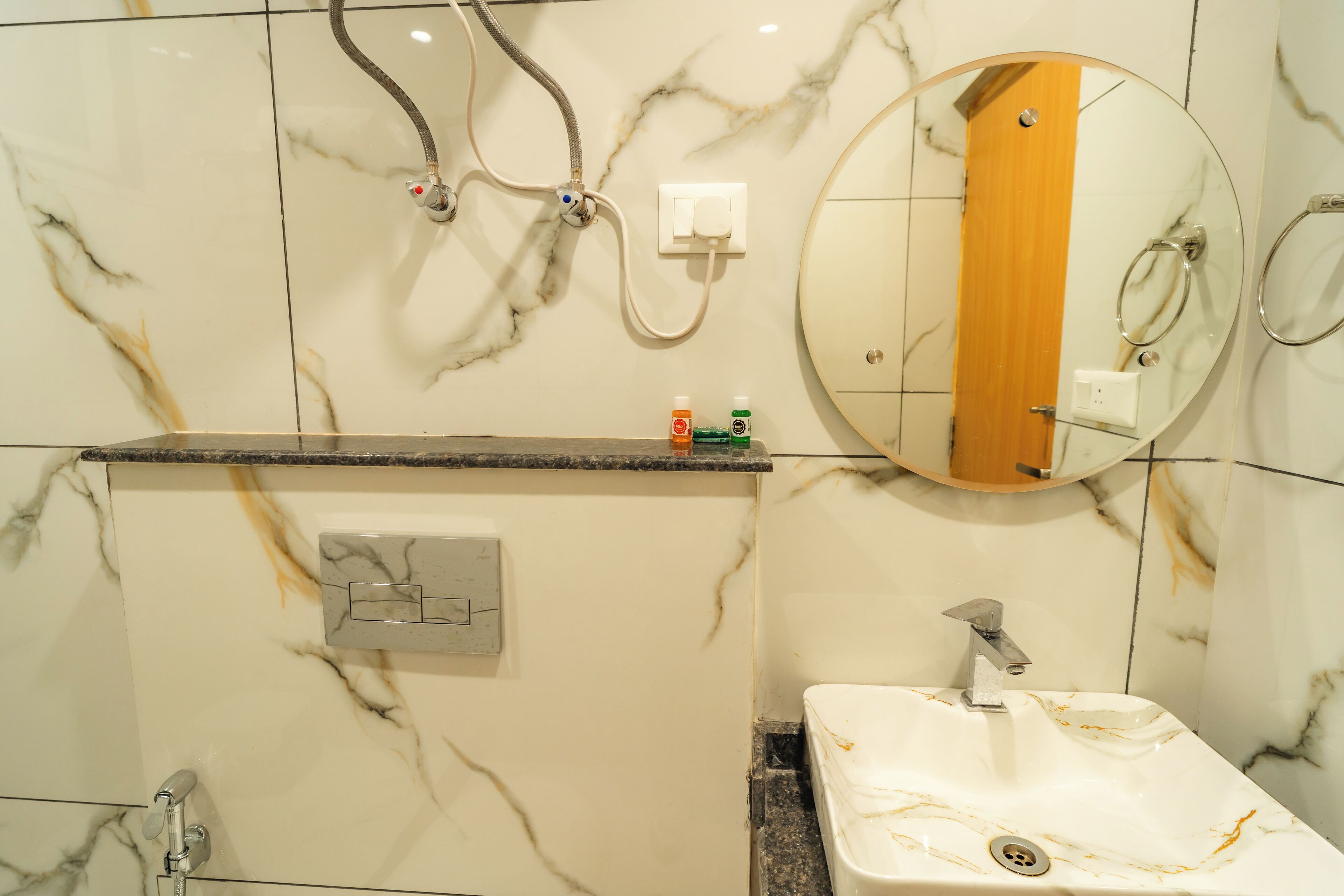 A bathroom with a marble wall, a sink, a mirror, and a shower.