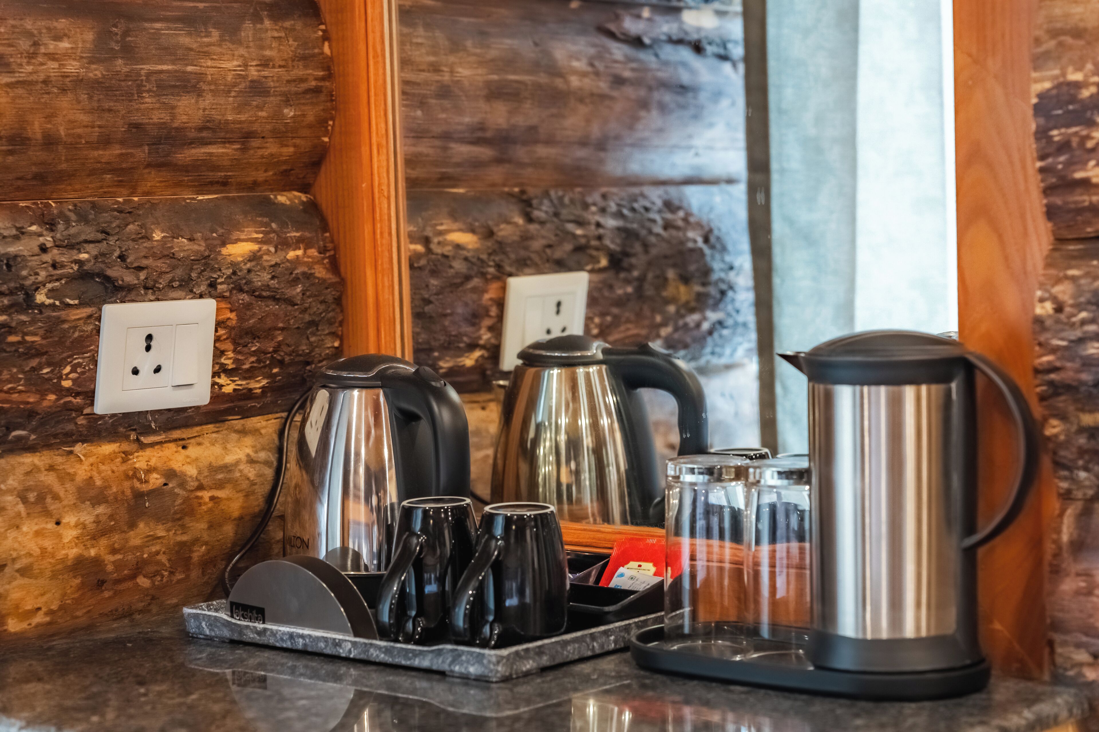 A kitchen counter with a coffee maker, kettles, and mugs.