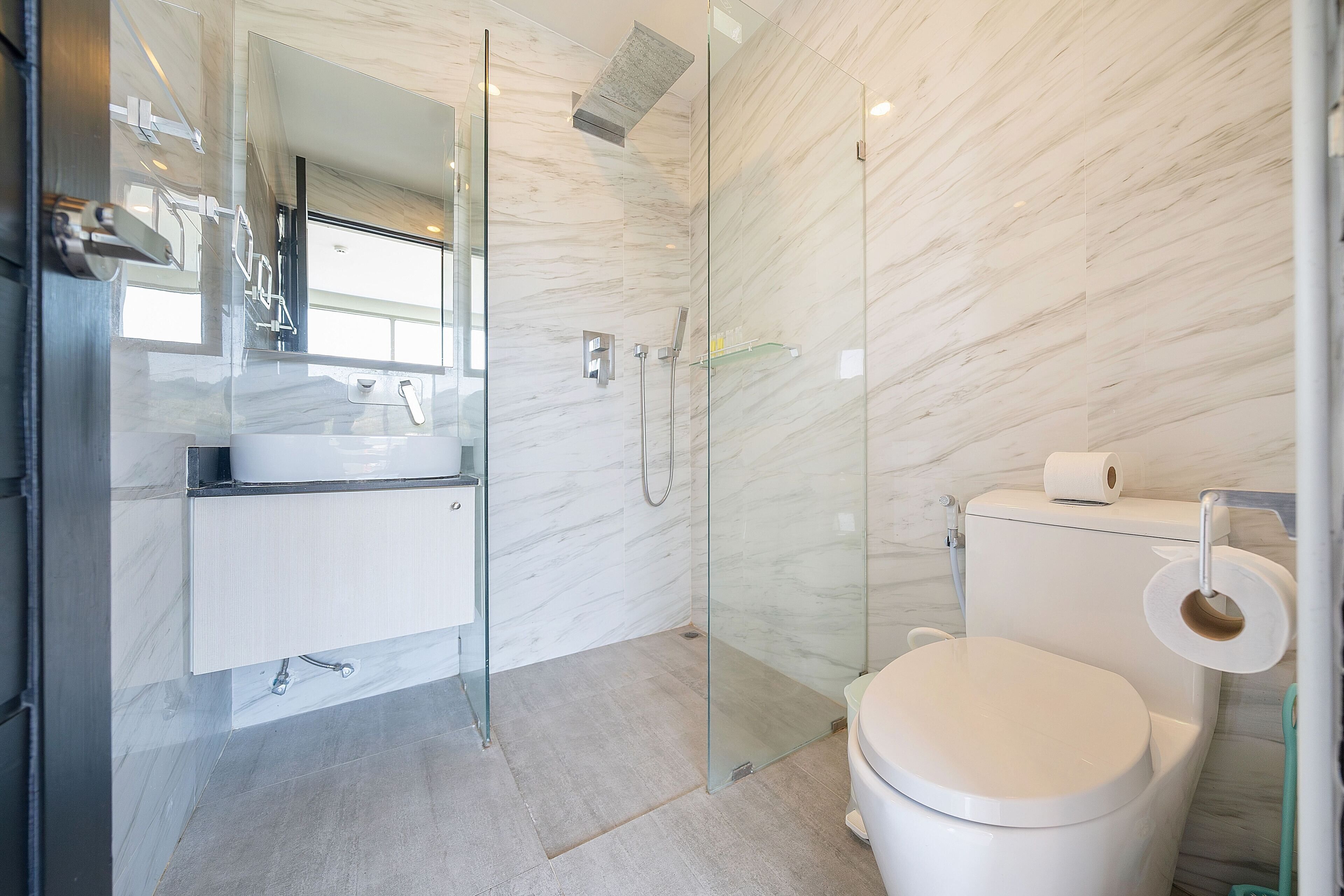 A modern bathroom with a glass shower enclosure, a white toilet, and a marble wall.