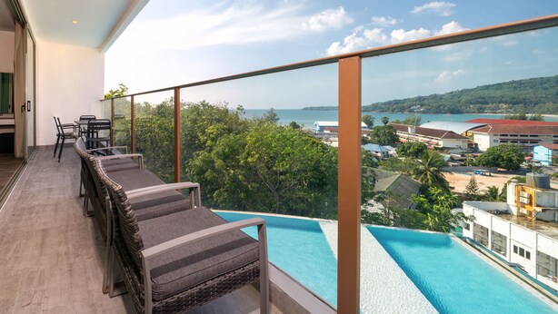 Ein Balkon mit Korbmöbeln, Blick auf einen Pool und die Küste.