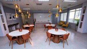 A modern conference room with round tables and orange chairs, large windows, and hanging pendant lights. - Cozy 4BR Apt@Brickell, free parking (Miami)