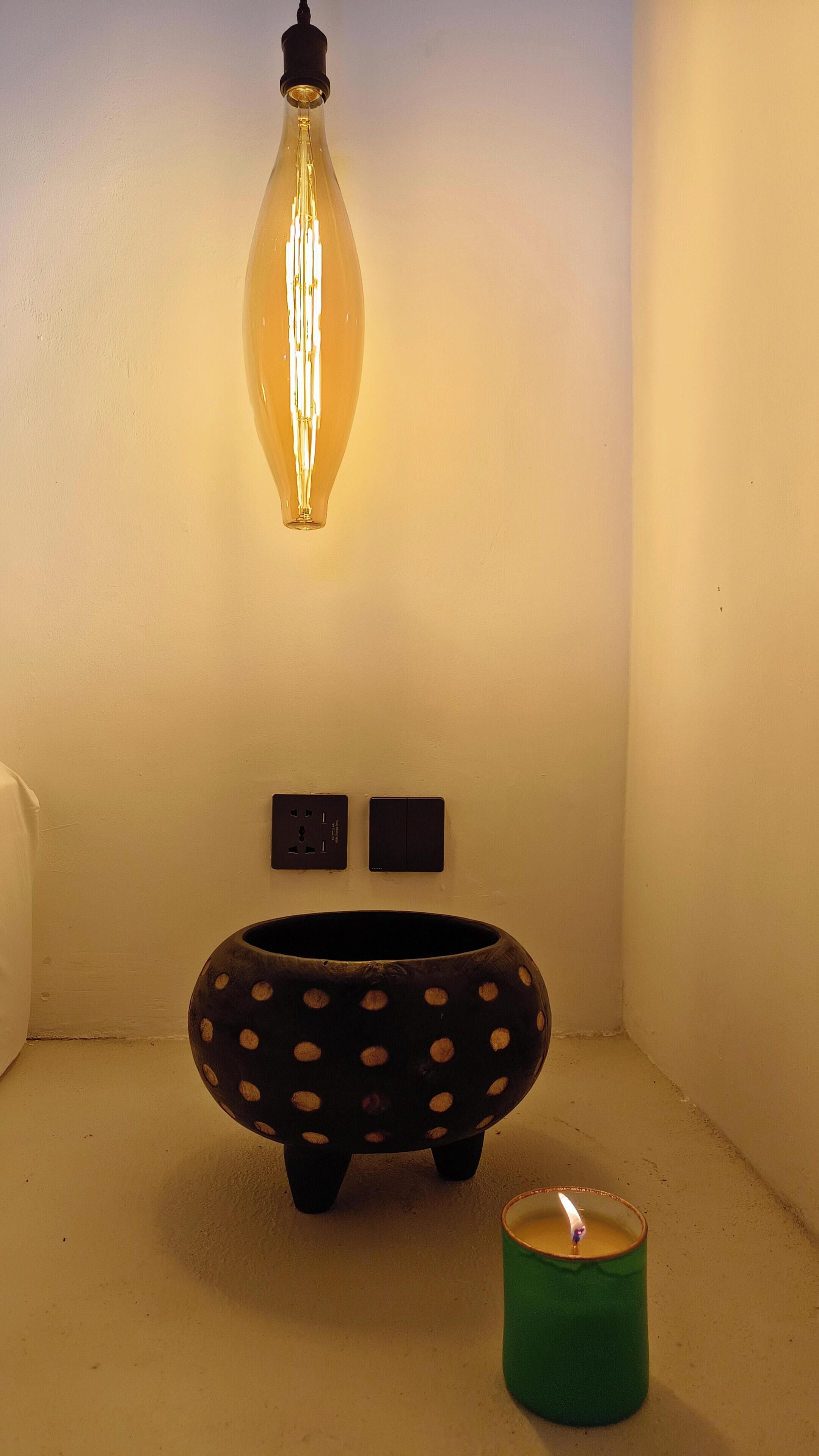 A room with a hanging light fixture, a polka-dotted bowl, and a lit candle.