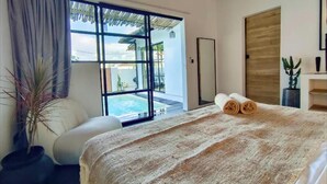Ein Schlafzimmer mit einem großen Bett, Blick auf einen Pool und einer Glastür zu einem Außenbereich.