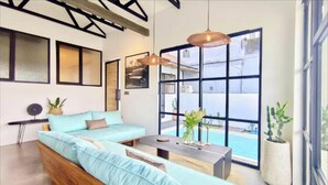 Ein modernes Wohnzimmer mit einer Couch, einem Couchtisch und einem großen Fenster mit Blick auf einen Pool.