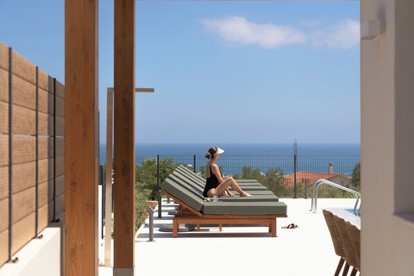 Une personne assise sur une chaise longue, face à la mer.