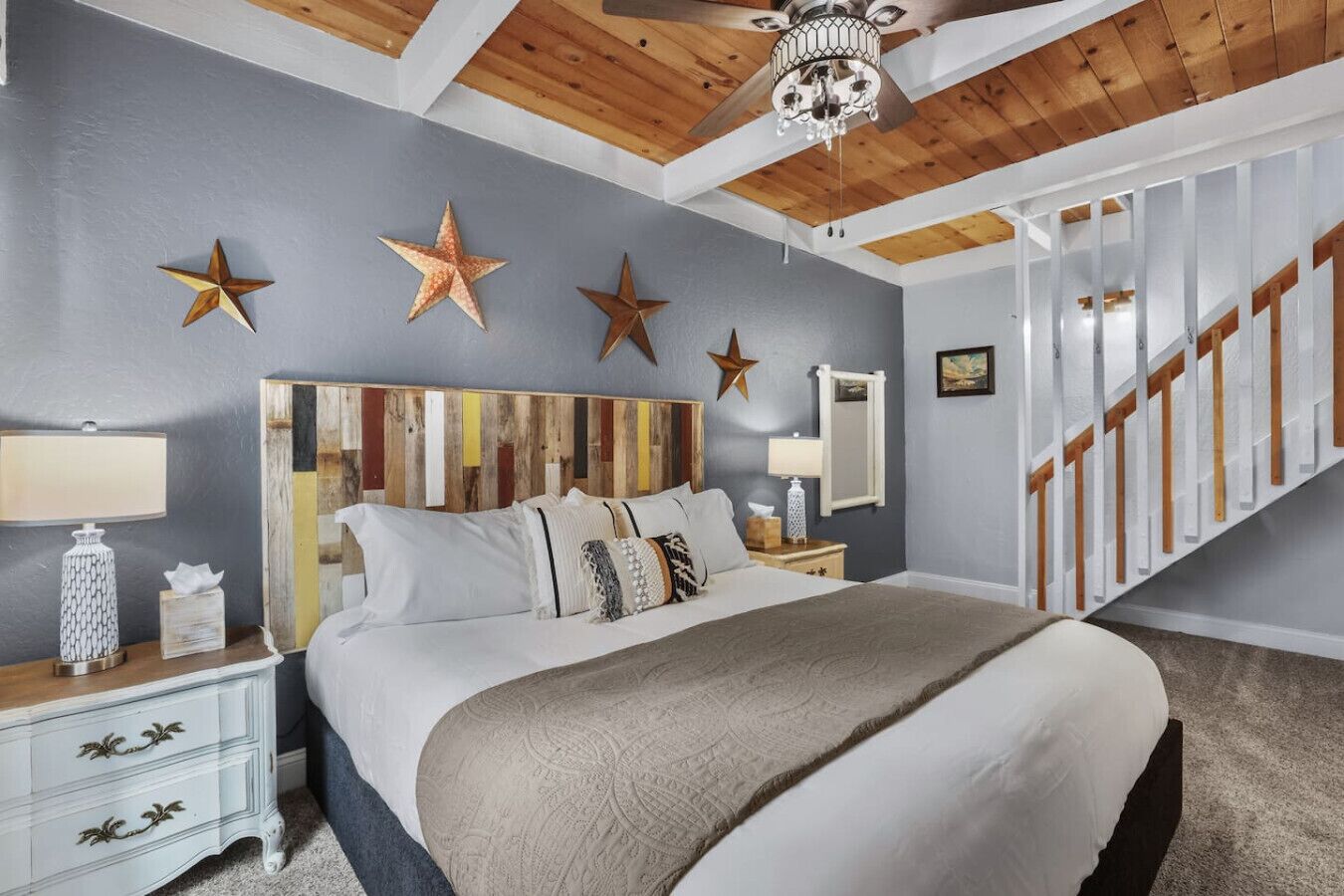 A bedroom with a wooden headboard, a bed with multiple pillows, a nightstand with a lamp, and a staircase.