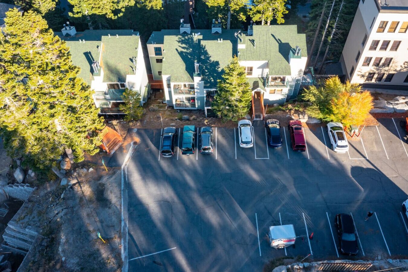 An aerial view of a parking lot with several cars parked, surrounded by trees and buildings with green roofs.