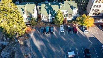 An aerial view of a parking lot with several cars parked, surrounded by trees and buildings with green roofs.
