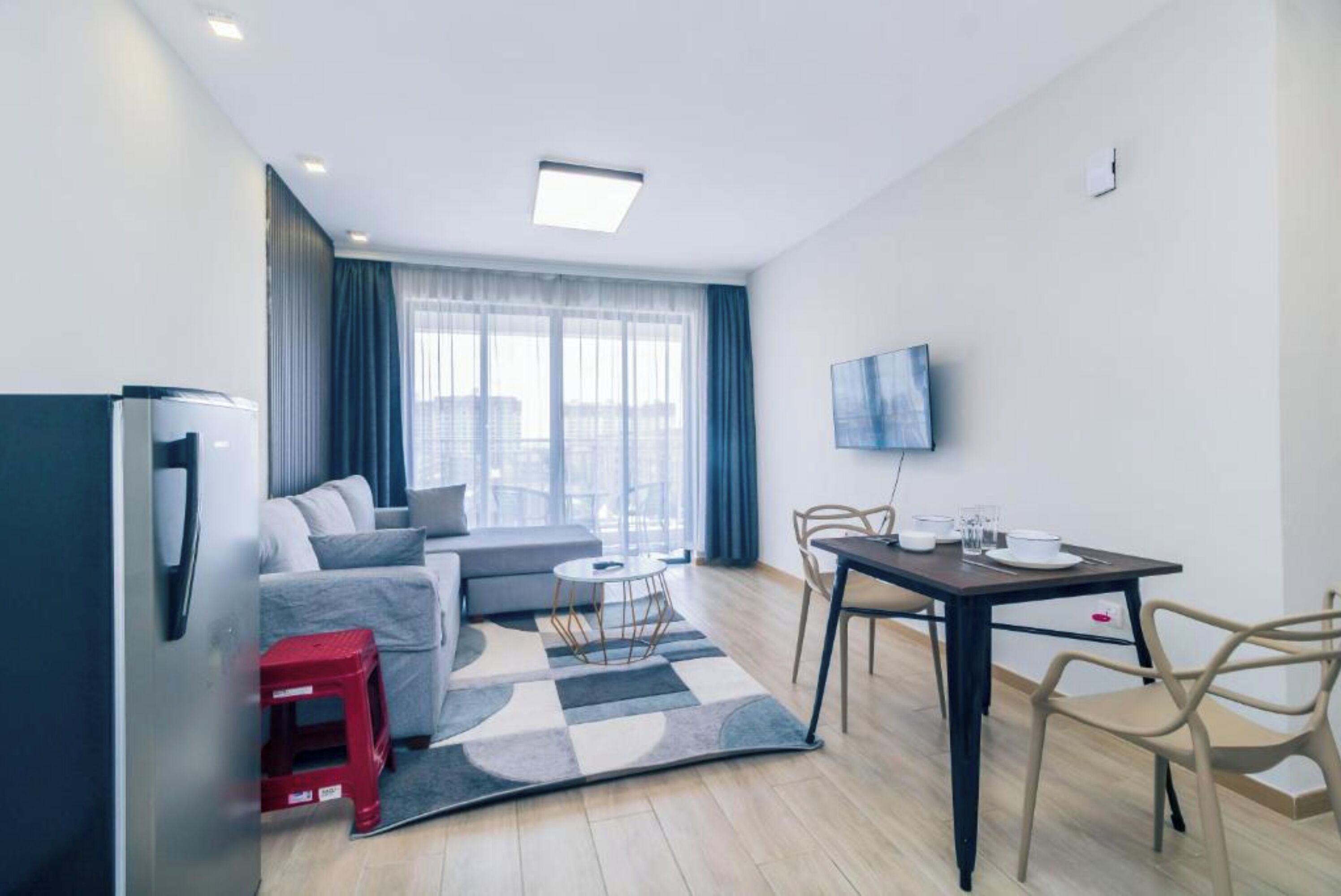 A modern living room with a sofa, a dining table, and a TV mounted on the wall.