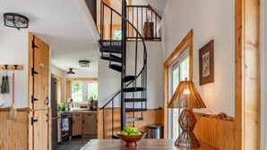 A modern kitchen with a wooden bench, a spiral staircase, and a dining table with a bowl of fruit. - Tiny Home with Spectacular Views & FP (Parksville)