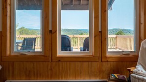 A room with three large windows offering views of a deck and surrounding greenery. - Tiny Home with Spectacular Views & FP (Parksville)