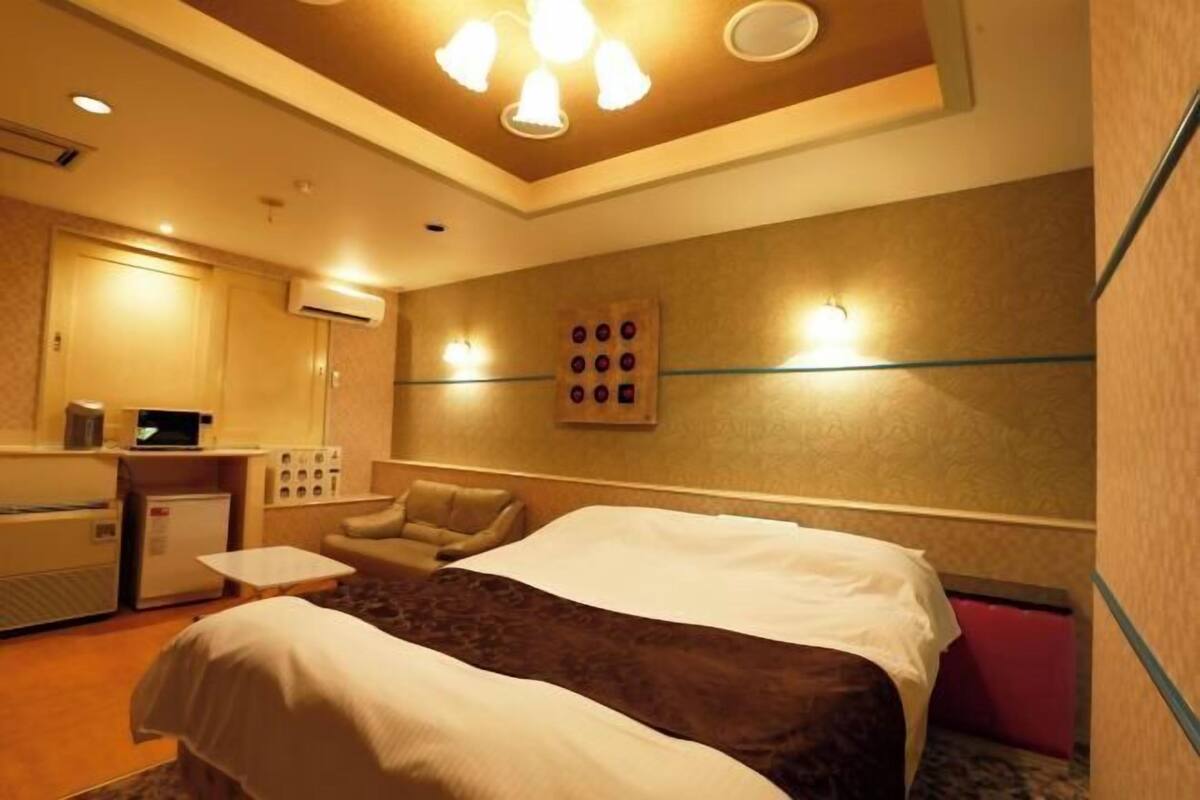 A hotel room with a bed, a desk with a computer, a chair, and a wall-mounted clock.