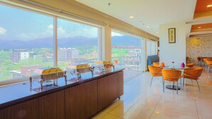 A modern hotel lobby with a large window offering a city view, a reception desk, and orange chairs around a round table. - LivBox Dehradun (Dehradun)