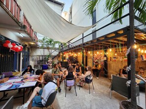 An outdoor seating area with tables and chairs, a mural on the wall, and a mix of indoor and outdoor elements. - AREA81 HIDEOUT Hostel Khaosan (Bangkok)