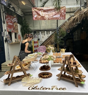 Eine Auswahl an glutenfreien Speisen auf einem Festival, darunter verschiedene Backwaren, mit einem Banner mit der Aufschrift 'Gluten Free Gourmet Fest'.