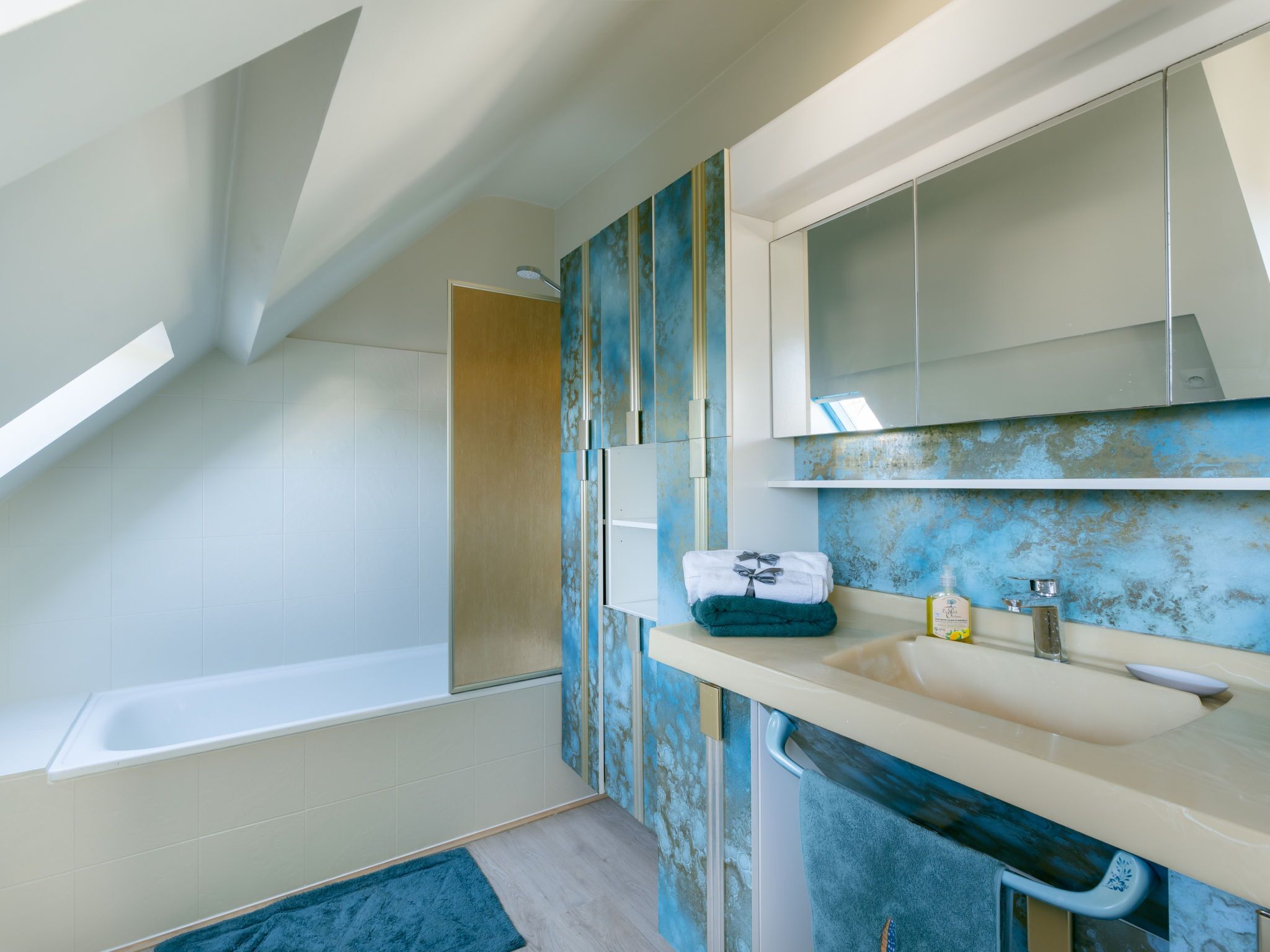 Ein modernes Badezimmer mit Oberlicht, einer Badewanne, einem Waschbecken inklusive Spiegel und einer Wand mit blauen Fliesen.