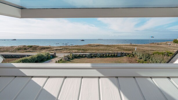 Une vue depuis une pièce dont le plafond est en verre, donnant sur une plage où se trouvent des bateaux, avec un ciel dégagé.