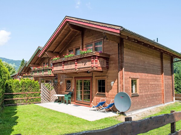 A wooden chalet with a balcony, a patio with chairs and a table, and a satellite dish.