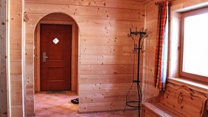 Un interior de madera con puerta, perchero, banco y ventana con cortinas.