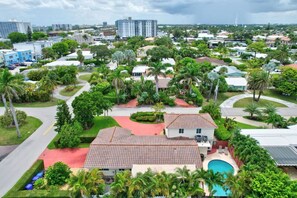 Zona residencial con una casa grande que tiene piscina, rodeada de abundante vegetación y palmeras.