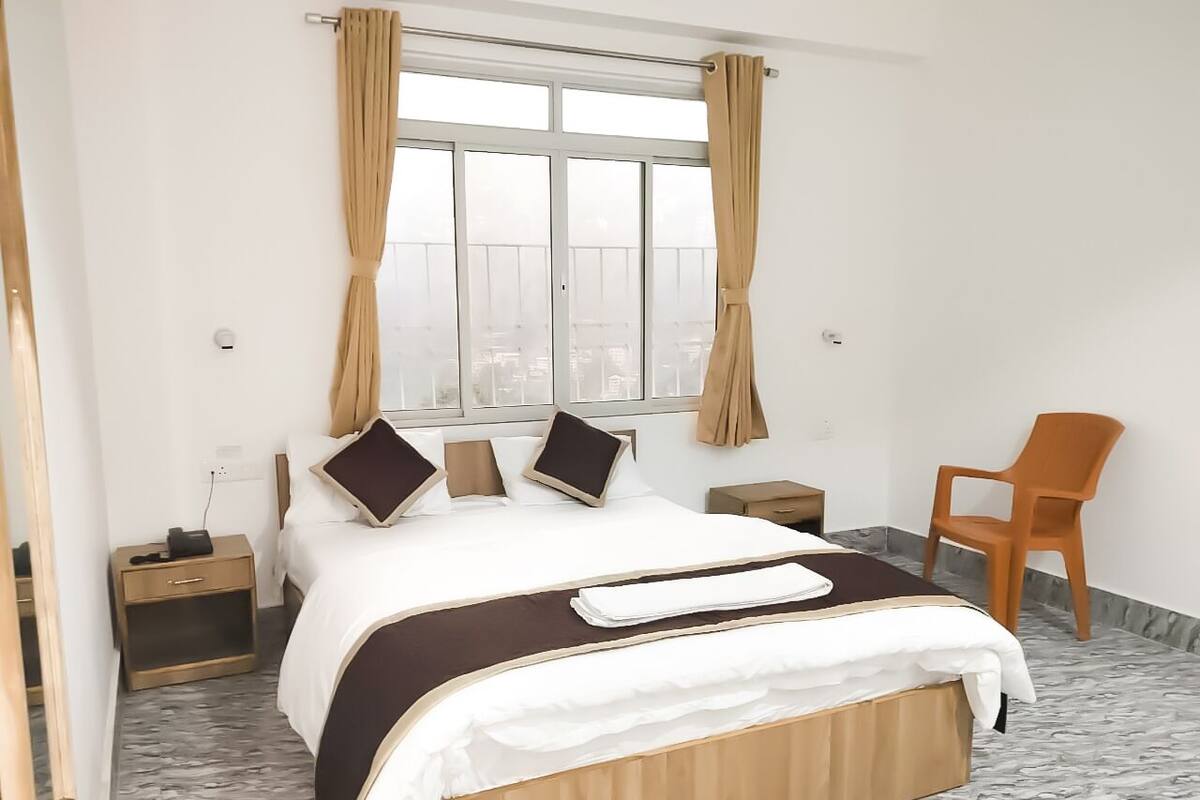 A hotel room with a bed, a chair, a nightstand, and a window with curtains.