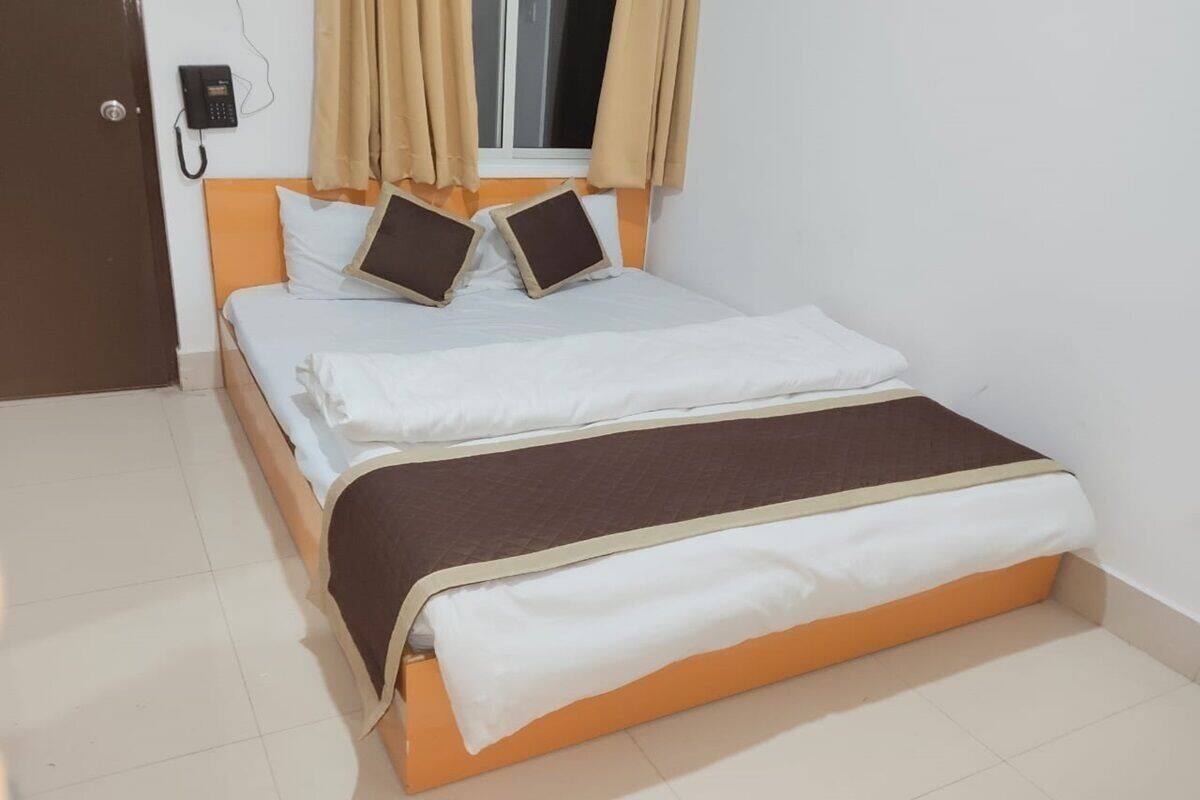 A neatly made bed with a brown and white bedspread, a wooden headboard, and beige curtains on a window.