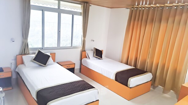 A hotel room with two beds, a desk, and a window with curtains. - Hotel East Inn (Gangtok)