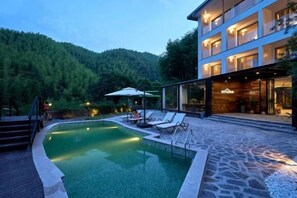 A modern hotel with a swimming pool, outdoor seating, and a forested backdrop. - Rest Valley (Deqing)