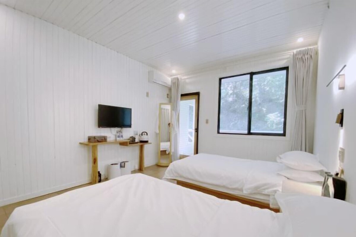 A hotel room with two beds, a TV, a window with curtains, and a small shelf with toiletries.