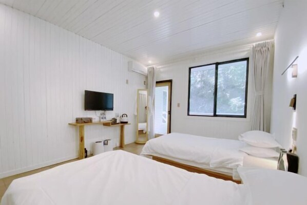 A hotel room with two beds, a TV, a window with curtains, and a small shelf with toiletries. - Rest Valley (Deqing)