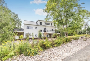 A two-story house with a balcony, surrounded by greenery and a stone pathway.