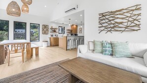 Een moderne woonkamer met een witte bank, een houten salontafel en een eethoek met een houten tafel en stoelen.