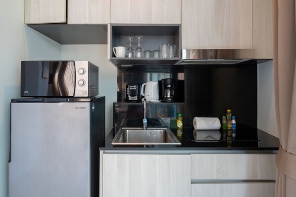 A compact kitchen with a refrigerator, microwave, coffee maker, and a sink.