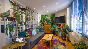 Ein modernes Wohnzimmer mit einem grauen Sofa, bunten Kissen, einem Couchtisch und einem Bücherregal voller Bücher und Dekoration.