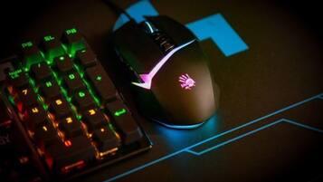 Un ratón para juegos con un logotipo en la parte superior, un teclado mecánico con iluminación RGB y un tapete para ratón con diseños geométricos azules.