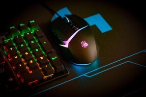 A gaming mouse with a logo on the top, a mechanical keyboard with RGB lighting, and a mouse pad with blue geometric designs. - Wuzhen Chaifeng Homestay (Tongxiang)