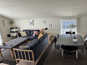 En moderne stue med en hjørnesofa, et spisebord og et stort vindue.